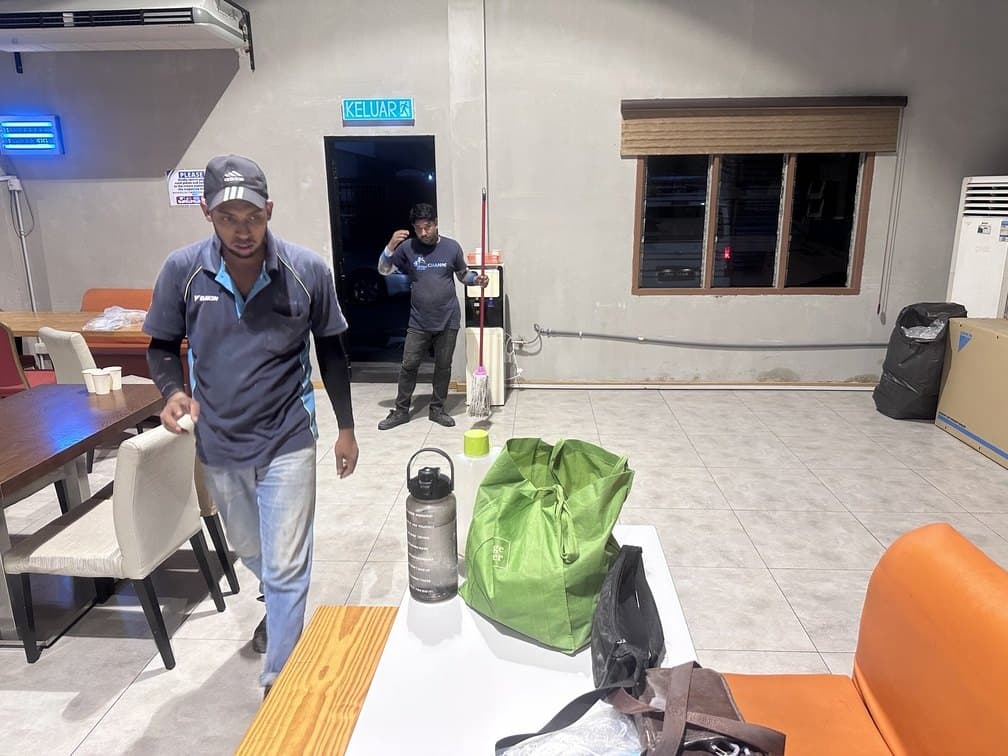 Two CASS technicians in company uniform working in a hospital cafeteria while the room remains in use.