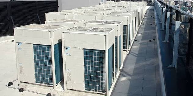 Rows of Daikin VRV condensing units laid out in ranks across a flat roof deck, with a building parapet running down one side.