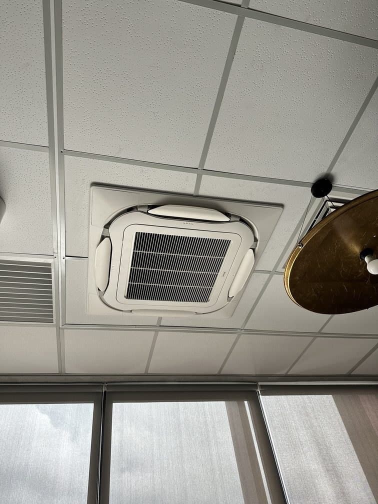 A ceiling cassette set flush into a suspended office ceiling beside a window line.