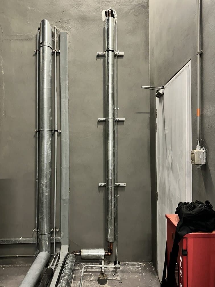 Two insulated refrigerant risers running floor to ceiling in a service shaft, clipped at regular intervals.