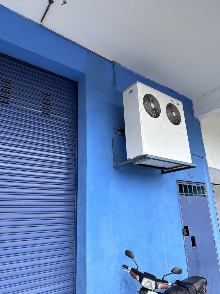 A condensing unit bracket-mounted high on the building frontage, clear of the roller shutter below.