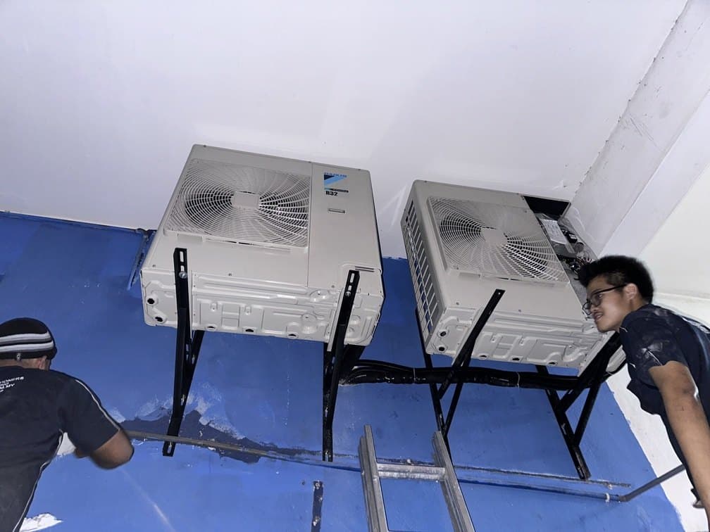 Two CASS installers setting a pair of outdoor condensing units onto wall brackets.