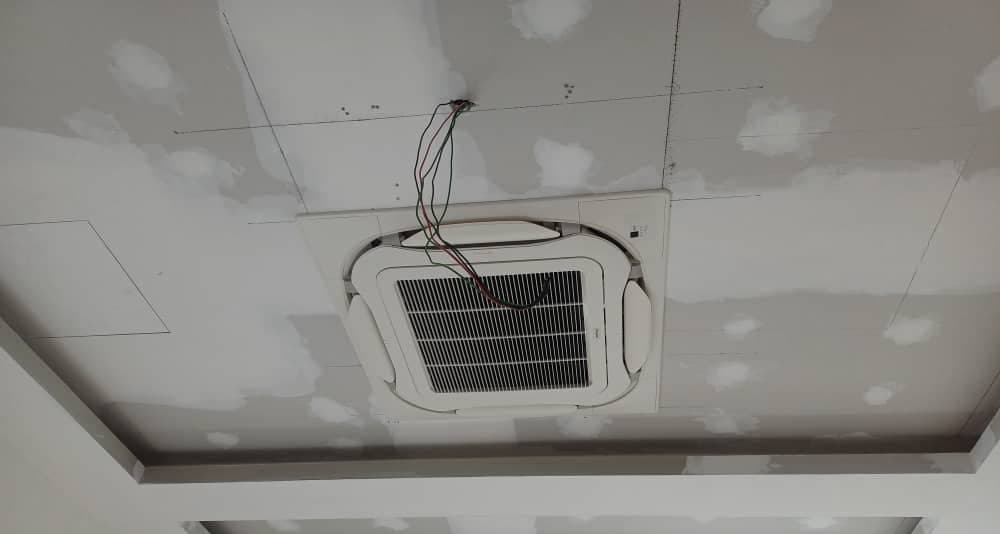 A ceiling cassette installed within a coffered ceiling detail, control wiring still exposed.
