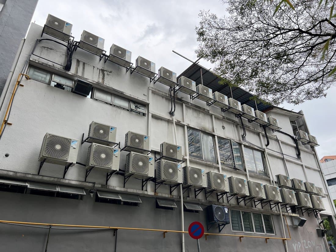 A shophouse rear elevation carrying rows of outdoor condensing units on wall brackets across several storeys.